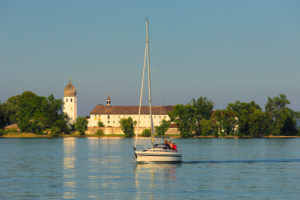 Segelboot auf dem Chiemsee vor der Fraueninsel mit Kloster Frauenwöth bei Sonnenuntergang, Oberbayern, Deutschland Segelboot auf dem Chiemsee vor der Fraueninsel mit Kloster Frauenwöth bei Sonnenuntergang, Oberbayern, Deutschland