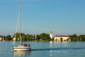 Segelboot auf dem Chiemsee vor der Fraueninsel mit Kloster Frauenwöth bei Sonnenuntergang, Oberbayern, Deutschland Segelboot auf dem Chiemsee vor der Fraueninsel mit Kloster Frauenwöth bei Sonnenuntergang, Oberbayern, Deutschland