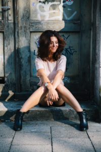 Young, attractive, brunette woman sitting in front of door with graffiti, cheerful, overexcited, shaking her hair Young, attractive, brunette woman sitting in front of door with graffiti, cheerful, overexcited, shaking her hair