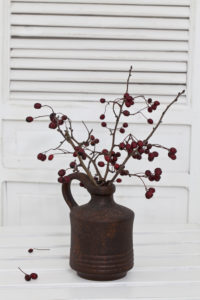 A rustic winter or Christmas deocoration in a white interior, with red berry twigs in a brown vase A rustic winter or Christmas deocoration in a white interior, with red berry twigs in a brown vase