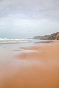 lonely, shallow sandy beach at the wild west coast of the portuguese algarve with rough cliffs lonely, shallow sandy beach at the wild west coast of the portuguese algarve with rough cliffs