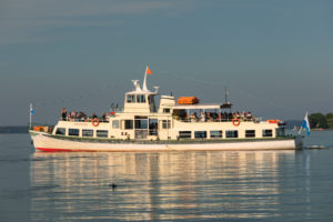 Ausflugsschiff auf dem Chiemsee vor der Fraueninsel bei Sonnenuntergang, Oberbayern, Deutschland Ausflugsschiff auf dem Chiemsee vor der Fraueninsel bei Sonnenuntergang, Oberbayern, Deutschland