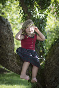Child with ivy tendril around its head, sitting in an apple tree Child with ivy tendril around its head, sitting in an apple tree