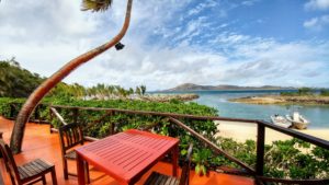 Red table and chairs on terrace on white sand beach, two boats in the sea, Fiji Red table and chairs on terrace on white sand beach, two boats in the sea, Fiji