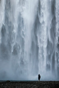 Person with black rain jacket in front of Skógafoss waterfall, Suðurland, Iceland Person with black rain jacket in front of Skógafoss waterfall, Suðurland, Iceland