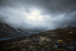 Three illuminated tents in a gloomy mountain landscape with a dramatic cloud mood, Jotunheimen, Norway Three illuminated tents in a gloomy mountain landscape with a dramatic cloud mood, Jotunheimen, Norway