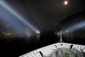 Cruise on the coast of Norway, Lofoten archipelago, narrow channel in the Trollfjord at night, illumination with on-board spotlights, moonlit night