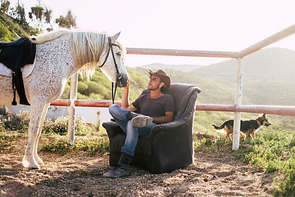 Bildagentur Mauritius Images Caucasian Man Enjoy His Horse Resting On A Seats Outdoor In The Countryside Alternative Lifestyle In Contact With Animals And Nature Dog In The Background