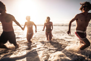 Group of beautiful millennial alternative young people have fun and enjoy the summer holiday vacation together in friendship running in the water of the ocean with sun in backlight Group of beautiful millennial alternative young people have fun and enjoy the summer holiday vacation together in friendship running in the water of the ocean with sun in backlight
