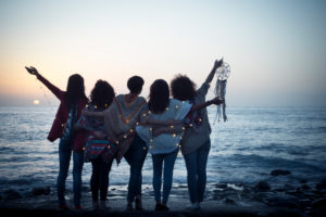 Romantic and dreamer concept image with five friends women hug each other viewed from back looking at the sunset holiding light - love freedom and wanderlust for group of people Romantic and dreamer concept image with five friends women hug each other viewed from back looking at the sunset holiding light - love freedom and wanderlust for group of people