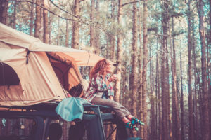 Happy free alternatie vacation traveler people - cute blonde sit down on the roof of the car with tent drinking coffee and enjoying the beauty of the forest around - wanderlust lifestyle girl Happy free alternatie vacation traveler people - cute blonde sit down on the roof of the car with tent drinking coffee and enjoying the beauty of the forest around - wanderlust lifestyle girl
