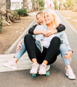 Happy young people couple of friends girls have fun together riding a skateboard on the road for outdoor leisure funny activity - friendship and craziness lifestyle concept for alternative millennial Happy young people couple of friends girls have fun together riding a skateboard on the road for outdoor leisure funny activity - friendship and craziness lifestyle concept for alternative millennial