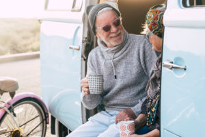 two happy seniors and mature married couple travelling together the worls with a blue and white van - sitting on the van with a cup of coffee or tea - elderly and retired travel lifestyle two happy seniors and mature married couple travelling together the worls with a blue and white van - sitting on the van with a cup of coffee or tea - elderly and retired travel lifestyle