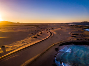 Beautiful aerial view of coast beach during the sunset -blue ocean and yellow sand and desert with sun light come from montains in background -travel and vacation concept Beautiful aerial view of coast beach during the sunset -blue ocean and yellow sand and desert with sun light come from montains in background -travel and vacation concept
