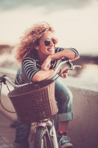 Cheerful trendy young adult caucasian woman sitting on a bike and smiling - beautiful female portrait - concept of outdoor leisure activity and happiness and joyful lifestyle Cheerful trendy young adult caucasian woman sitting on a bike and smiling - beautiful female portrait - concept of outdoor leisure activity and happiness and joyful lifestyle