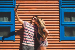 Young beautiful caucasian people couple take a slefie picture together with a kiss and smile - technology and social media pictures concept - coloured background Young beautiful caucasian people couple take a slefie picture together with a kiss and smile - technology and social media pictures concept - coloured background