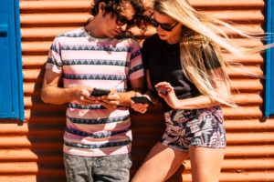 Young caucasian couple use modern cellular phone device together sharing contents with app and technology - outdoor people in leisure activity with internet and social media Young caucasian couple use modern cellular phone device together sharing contents with app and technology - outdoor people in leisure activity with internet and social media