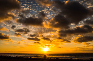 Romantic couple sit down at the beach enjoying the coloured beautiful sunset - concep of hope and love for people and nature - outdoor romance activity with silhouette and ocean Romantic couple sit down at the beach enjoying the coloured beautiful sunset - concep of hope and love for people and nature - outdoor romance activity with silhouette and ocean