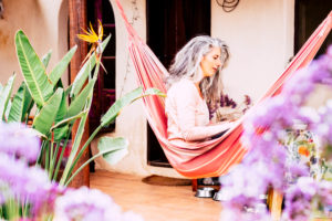 Long grey and white hair adult woman alternative look have relax at home in the garden sitting on a coloured hammock alone Long grey and white hair adult woman alternative look have relax at home in the garden sitting on a coloured hammock alone
