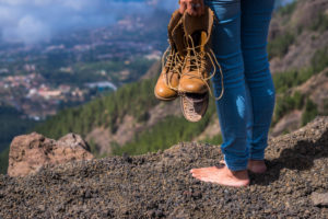 Travel and wanderlust lifestyle concept with barefoot woman stand up with broken shoes on hands looking at the view on the top of the mountain Travel and wanderlust lifestyle concept with barefoot woman stand up with broken shoes on hands looking at the view on the top of the mountain