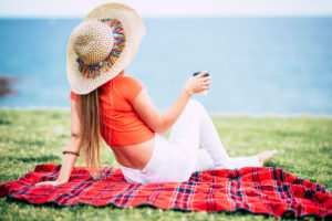 Summer and tourist concept with trendy caucasian woman sit down on the grass and enjoy looking the blue ocean drinking a tea or coffee alone - coloured lifestyle and travel Summer and tourist concept with trendy caucasian woman sit down on the grass and enjoy looking the blue ocean drinking a tea or coffee alone - coloured lifestyle and travel