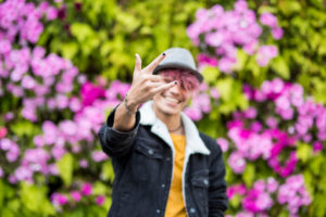 Happy cheerful handsome trendy alternative young man teenager portrait smiling on camera with coloured flower park background - diversity and youthful people with joy Happy cheerful handsome trendy alternative young man teenager portrait smiling on camera with coloured flower park background - diversity and youthful people with joy
