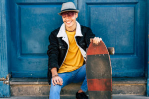 Cheerful and happy teenager sit down outside home with blue old door in background - city urban lifestyle and trendy generation z people concept - youthful and joy model with skateboard Cheerful and happy teenager sit down outside home with blue old door in background - city urban lifestyle and trendy generation z people concept - youthful and joy model with skateboard