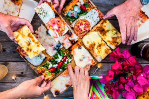 Close up view of table full of caucasian group people hands taking italian pizza and eat together in friendship for celebration party - concept of happiness and friends at home or restaurant Close up view of table full of caucasian group people hands taking italian pizza and eat together in friendship for celebration party - concept of happiness and friends at home or restaurant