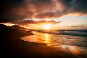 Wonderful timeless sunset at the beach with dramatic clouds and waves - mountains in background and wild scenic place - golden and fire colors in a beauty of nature Wonderful timeless sunset at the beach with dramatic clouds and waves - mountains in background and wild scenic place - golden and fire colors in a beauty of nature