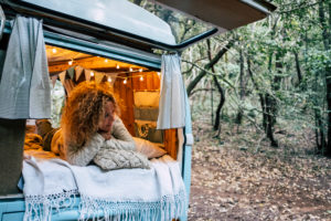 Happy free beautiful woman lay down and relax inside her blue van vehicle parked in the forest - people enjoying alternative travel and vacation or life options - female enjoying the camper van vacation Happy free beautiful woman lay down and relax inside her blue van vehicle parked in the forest - people enjoying alternative travel and vacation or life options - female enjoying the camper van vacation