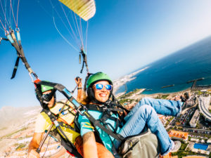 Cheerful happy woman to paraglyde experience with pilot - couple having fun in the air paraglyding over the city with coastline view - tourist and summer holiday vacation active people Cheerful happy woman to paraglyde experience with pilot - couple having fun in the air paraglyding over the city with coastline view - tourist and summer holiday vacation active people