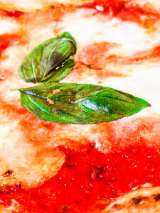 A detailed view of a margherita pizza with melted mozzarella, fresh tomato sauce, and fragrant basil leaves, baked to perfection with a thin crispy crust, showcasing the essence of Italian tradition