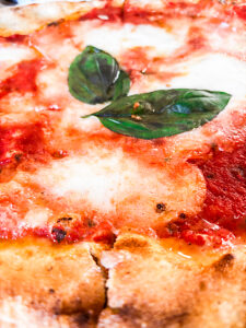 Close-up shot of a margherita pizza highlighting fresh basil, mozzarella cheese, and ripe tomatoes on a thin golden crust, reflecting the authentic flavors and simplicity of Mediterranean cuisine.