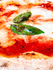 Detailed view of a margherita pizza featuring a crispy crust, fresh mozzarella, tomato sauce, and fragrant basil leaves, showcasing the iconic simplicity and flavors of Italian cuisine