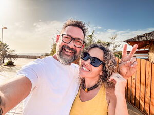 Smiling couple taking a selfie on a sunny beach during a summer holiday, enjoying the tropical atmosphere with blue ocean waves, golden sand, and clear sky creating a relaxing and scenic view