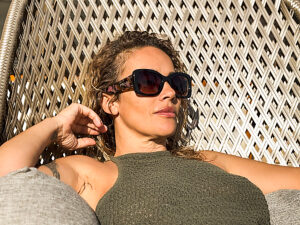 Beautiful adult woman sitting on a comfortable chair in a sunny garden during summer, wearing stylish sunglasses and embracing relaxation, tranquility, and the pleasant atmosphere of the outdoors