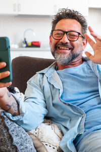 Happy adult 50s man staring at cell phone screen, enjoy videocall, on-line communication using modern tech and application, spend time alone at home, lead pleasant talk to family living abroad