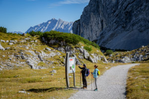 Man and woman hiking on road sign at Osterfelder at the foot of the Alpspitze, in the background the Wetterstein Mountains, blue sky, hiking trail, Garmisch-Partenkirchen, Upper Bavaria, Bavaria, southern Germany, Germany Man and woman hiking on road sign at Osterfelder at the foot of the Alpspitze, in the background the Wetterstein Mountains, blue sky, hiking trail, Garmisch-Partenkirchen, Upper Bavaria, Bavaria, southern Germany, Germany