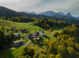 Wamberg with St. Anna's Church in autumn, aerial view with a view along the walk towards the Wetterstein Mountains with Alpspitze, Zugspitze and Waxensteine, blue sky, veil clouds, trees, Garmisch-Partenkirchen, Upper Bavaria, Bavaria, southern Germany, Germany Wamberg with St. Anna's Church in autumn, aerial view with a view along the walk towards the Wetterstein Mountains with Alpspitze, Zugspitze and Waxensteine, blue sky, veil clouds, trees, Garmisch-Partenkirchen, Upper Bavaria, Bavaria, southern Germany, Germany