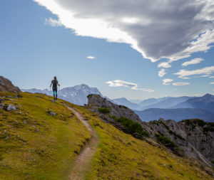 Young woman hiking towards Kramer looks towards the Wetterstein Mountains (with Zugspitze) and to the right the Ammergau Alps, blue sky, clouds, hiking trail, rock, Garmisch-Partenkirchen, Upper Bavaria, Bavaria, southern Germany, Germany Young woman hiking towards Kramer looks towards the Wetterstein Mountains (with Zugspitze) and to the right the Ammergau Alps, blue sky, clouds, hiking trail, rock, Garmisch-Partenkirchen, Upper Bavaria, Bavaria, southern Germany, Germany