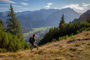 Young woman hiking towards Kramer in autumn with a view over Garmisch-Partenkirchen and Wetterstein Mountains with Alpspitze, Zugspitze, and Waxensteine, blue sky, clouds, hiking trail, trees, Garmisch-Partenkirchen, Upper Bavaria, Bavaria, southern Germany, Germany Young woman hiking towards Kramer in autumn with a view over Garmisch-Partenkirchen and Wetterstein Mountains with Alpspitze, Zugspitze, and Waxensteine, blue sky, clouds, hiking trail, trees, Garmisch-Partenkirchen, Upper Bavaria, Bavaria, southern Germany, Germany