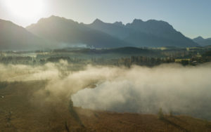 Aerial view mist at the Barmsee against the Karwendel mountains, blue sky, trees, lake shore, sun, back light, Krün, Garmisch-Partenkirchen, Upper Bavaria, Bavaria, southern Germany, Germany Aerial view mist at the Barmsee against the Karwendel mountains, blue sky, trees, lake shore, sun, back light, Krün, Garmisch-Partenkirchen, Upper Bavaria, Bavaria, southern Germany, Germany