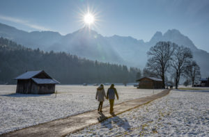 Man and woman on a winter walk on a dirt road in Garmisch-Partenkirchen, looking towards the Wetterstein Mountains with the Alpspitze and wax stones, wooden sticks, blue sky, sun, back light, trees, meadow, walking path, Garmisch-Partenkirchen, Upper Bavaria, Bavaria, southern Germany, Germany Man and woman on a winter walk on a dirt road in Garmisch-Partenkirchen, looking towards the Wetterstein Mountains with the Alpspitze and wax stones, wooden sticks, blue sky, sun, back light, trees, meadow, walking path, Garmisch-Partenkirchen, Upper Bavaria, Bavaria, southern Germany, Germany