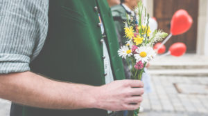 Ein Mann mit Trachtenhemd und Weste hält einen kleinen Blumenstrauß in der Hand, um zur Hochzeit zu gratulieren. Ein Mann mit Trachtenhemd und Weste hält einen kleinen Blumenstrauß in der Hand, um zur Hochzeit zu gratulieren.