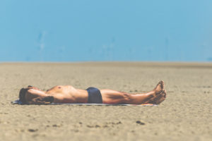 Mann mit Badehose liegt im Sand und sonnt sich, St.Peter Ording, Strandurlaub, im Hintergrund Windräder Mann mit Badehose liegt im Sand und sonnt sich, St.Peter Ording, Strandurlaub, im Hintergrund Windräder