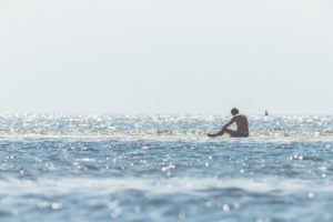 Mann mit Badehose sitzt im Wasser im Wattenmeer und beobachtet die Wellen und die kommende Flut. Mann mit Badehose sitzt im Wasser im Wattenmeer und beobachtet die Wellen und die kommende Flut.