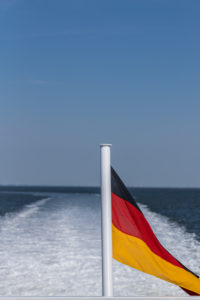 Eine deutsche Fahne, im Wind wehend, auf einem Schiff am Meer. Schwarz, Rot, Gold die Nationalfarben. Symbolbild Eine deutsche Fahne, im Wind wehend, auf einem Schiff am Meer. Schwarz, Rot, Gold die Nationalfarben. Symbolbild