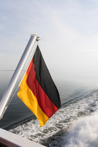 Eine deutsche Fahne, im Wind wehend, auf einem Schiff am Meer. Schwarz, Rot, Gold die Nationalfarben. Symbolbild Eine deutsche Fahne, im Wind wehend, auf einem Schiff am Meer. Schwarz, Rot, Gold die Nationalfarben. Symbolbild