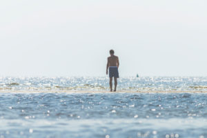 Beach recreation - man in swimming trunks looks out over the water and watches the waves. Beach recreation - man in swimming trunks looks out over the water and watches the waves.