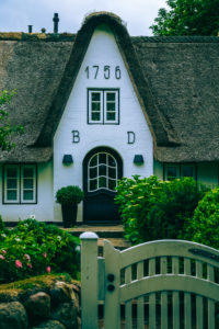 A garden gate in a stone wall and a front door of a house from 1756 on Sylt.